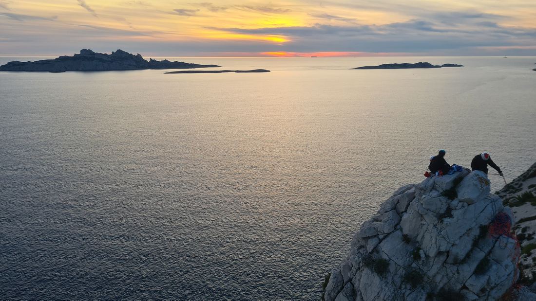 Deux grimpeurs sur le rocher face à la mer au coucher du soleil